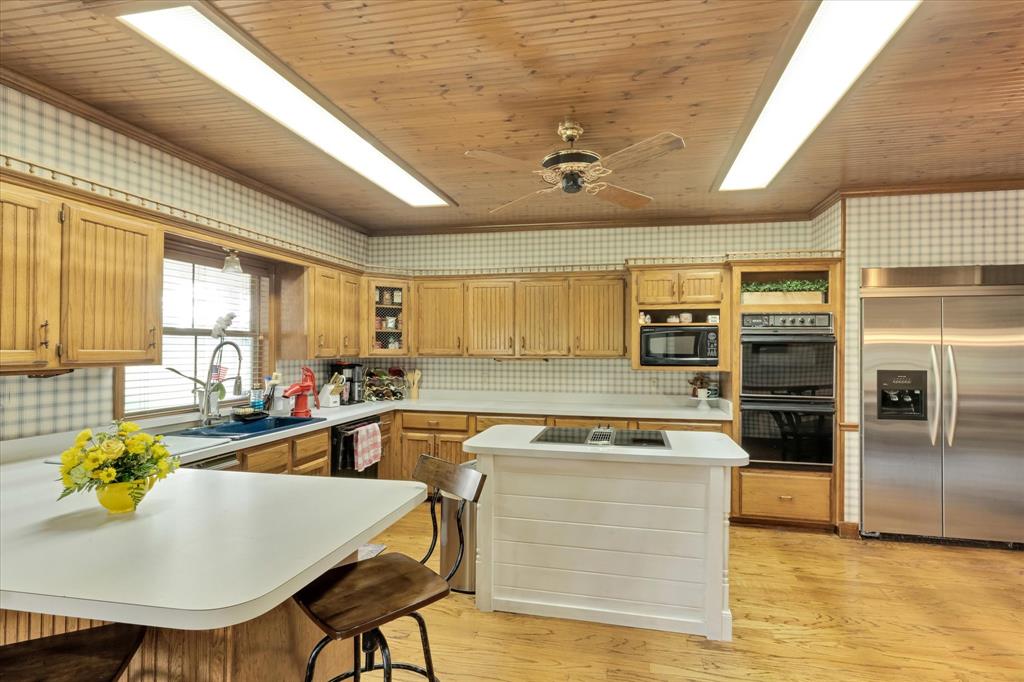 2717 Clear Lake Road Weatherford, TX 76087 - Photo 11 of 40 Kitchen featuring wood-finish flooring, wood-paneled ceiling, light wood cabinetry, stainless steel appliances, and a central island with an integrated cooktop. Sub-Zero built in refrigerator