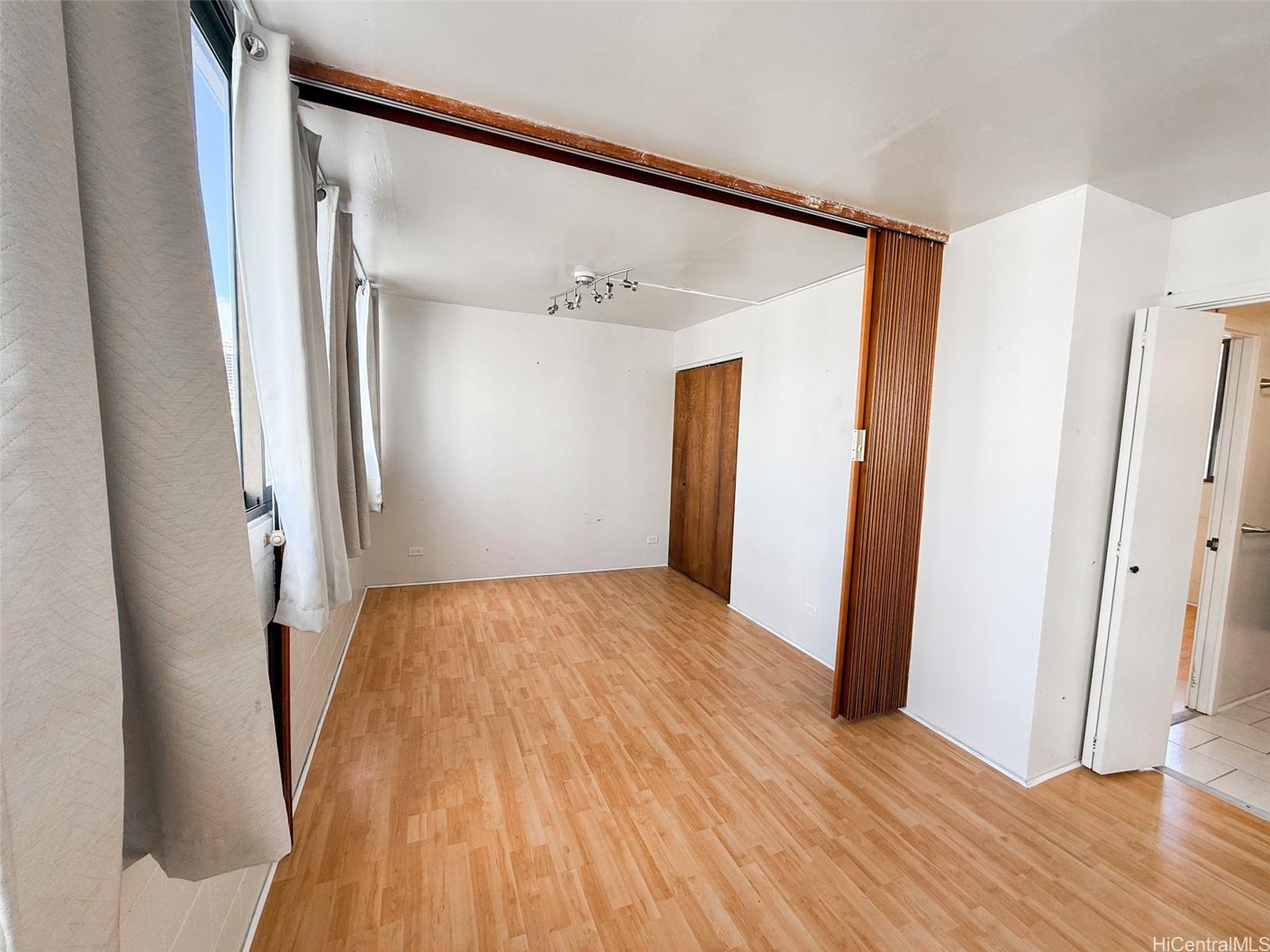 a view of an empty room with wooden floor and a bathroom
