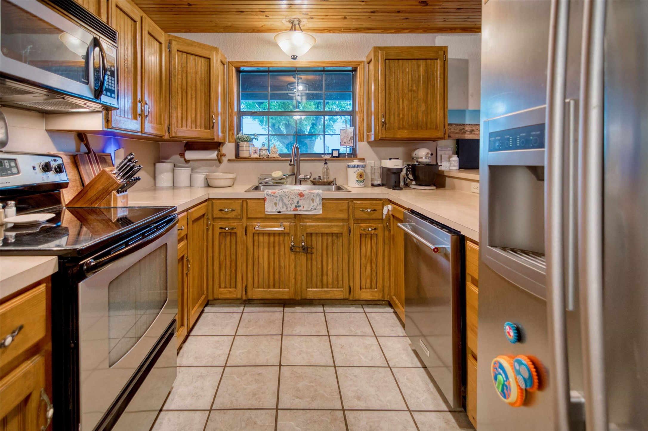 904 Bluebonnet Road Mason, TX 76856 - Photo 14 of 28 Kitchen featuring honey-toned wood cabinetry, U-shaped countertop, stainless steel appliances, tile flooring, and a wood-panel ceiling