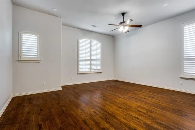 an empty room with wooden floor chandelier fan and windows