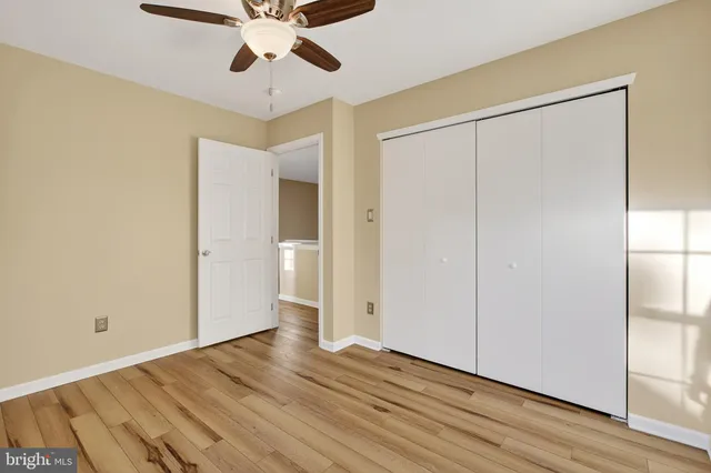a view of an empty room with wooden floor and a ceiling fan