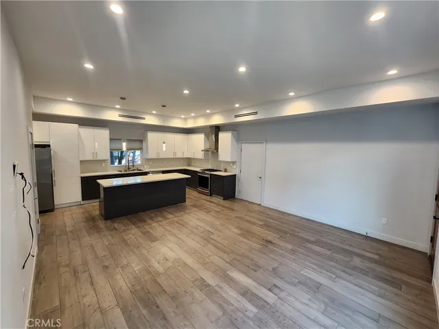 a large white kitchen with kitchen island a sink dishwasher a stove and a refrigerator with wooden floor