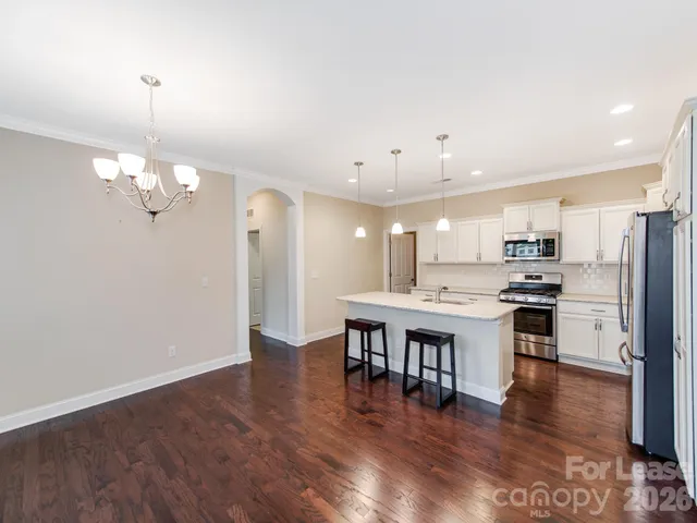 a kitchen with stainless steel appliances a dining table chairs stove refrigerator and cabinets