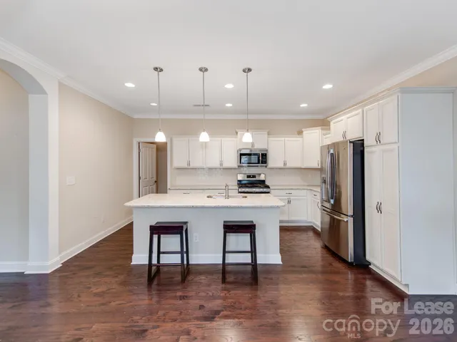 a kitchen with stainless steel appliances a dining table chairs refrigerator and microwave