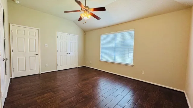an empty room with wooden floor chandelier fan and windows