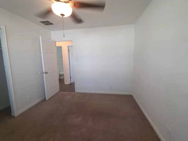 an empty room with a chandelier fan and wooden floor