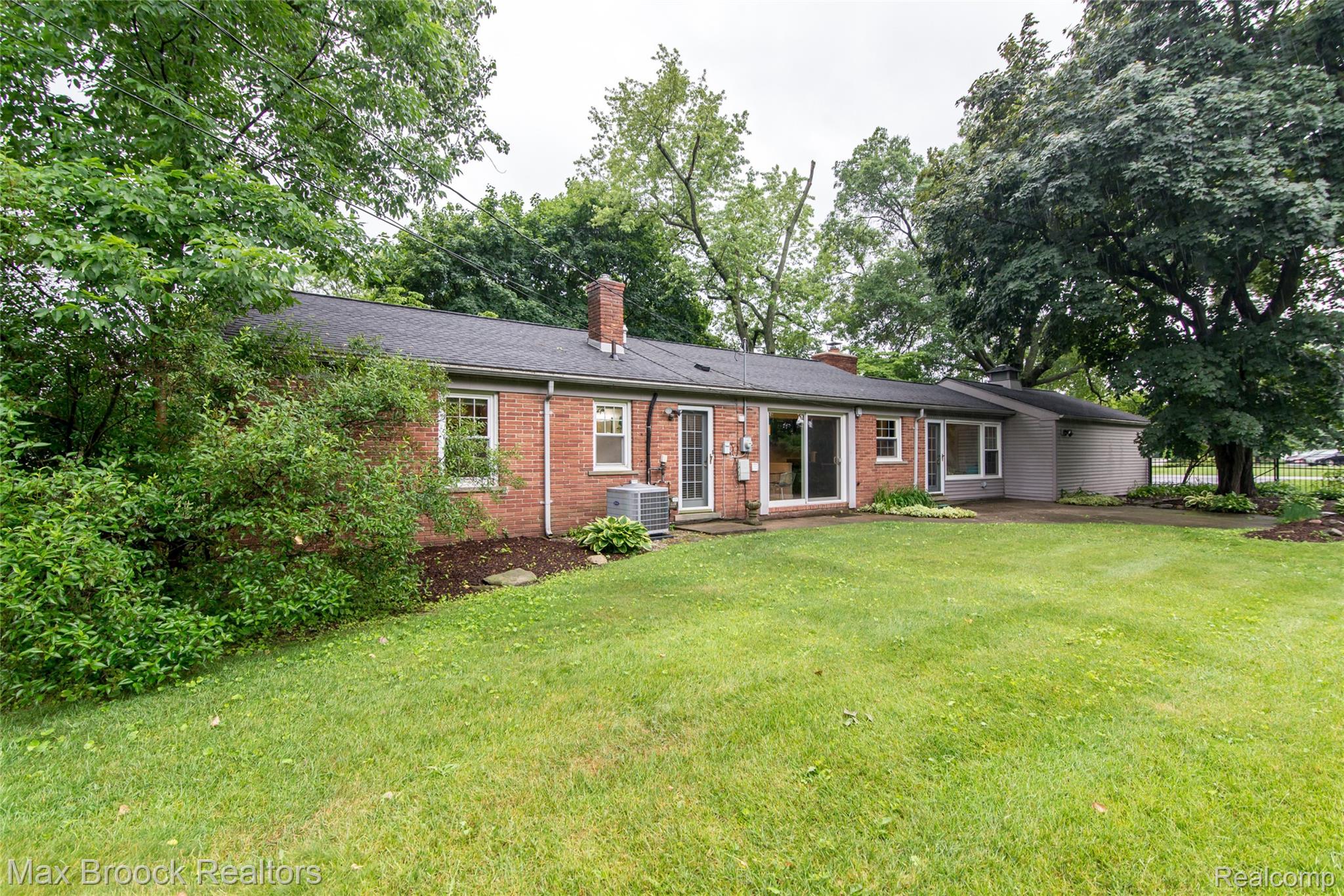 6799 East Dartmoor Road West Bloomfield, MI 48322 - Photo 33 of 36 Expansive rear lawn framed by mature trees, brick exterior, multiple windows, double glass doors, and a covered patio area
