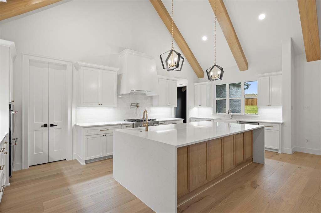 108 Bel Grand Road Haslet, TX 76052 - Photo 21 of 40 Dual tone kitchen with an island with sink, light stone counters, light wood-style floors, vaulted ceiling, and a chandelier