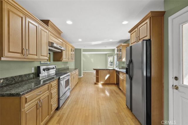 a kitchen with stainless steel appliances granite countertop a refrigerator a stove top oven a sink dishwasher and wooden cabinets with wooden floor