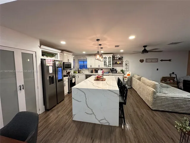 a large kitchen that has a lot of white cabinets a sink and stainless steel appliances
