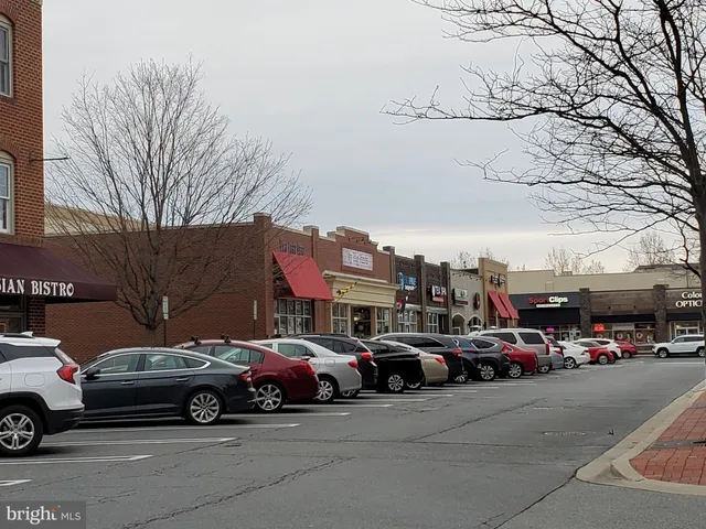 a view of road with card parked on side and retail shops