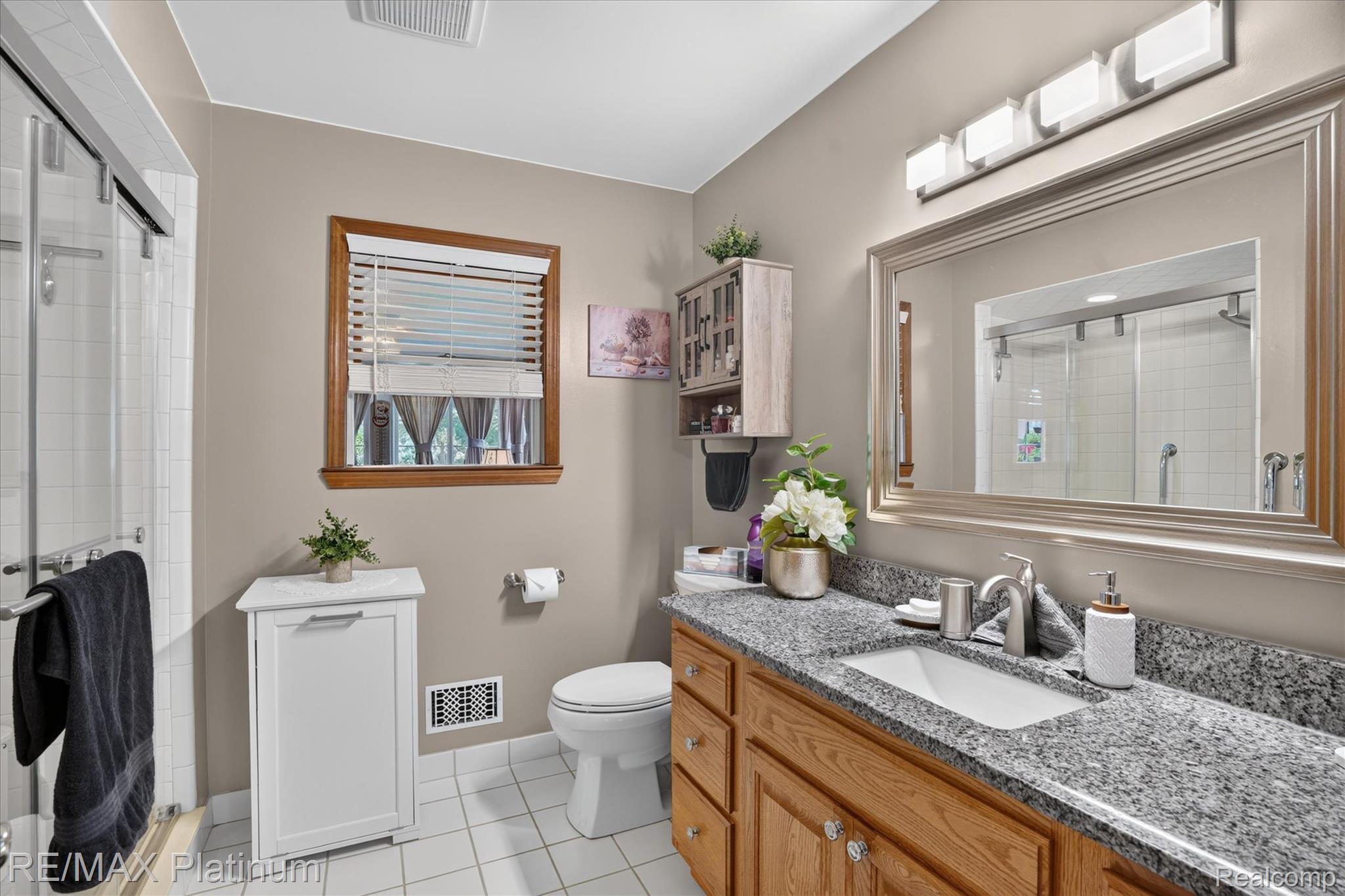 4457 Bradley Road Gregory, MI 48137 - Photo 20 of 79 Bathroom featuring a wood vanity with granite-style countertop and undermount sink, a framed mirror, a four-light vanity fixture, a window with wood trim, and a glass-enclosed shower with a sliding door
