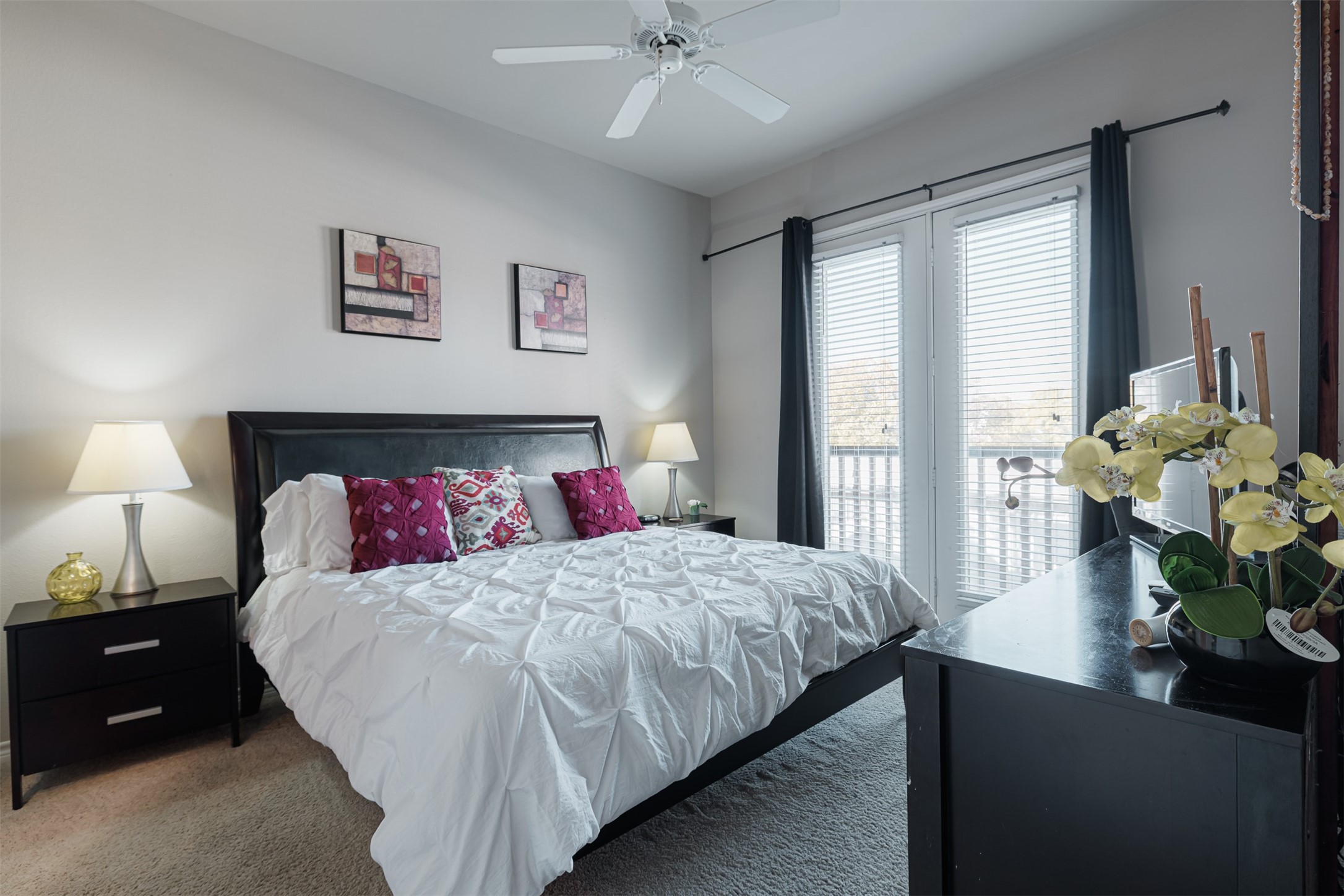Bright and inviting bedroom featuring a plush bed with vibrant accent pillows, elegant nightstands, and large windows for ample natural light.