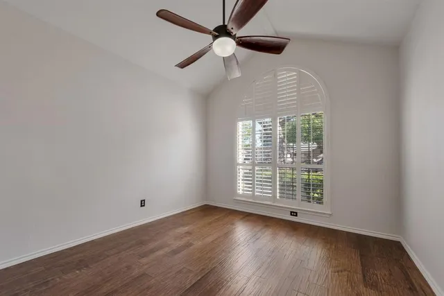 an empty room with wooden floor chandelier fan and windows