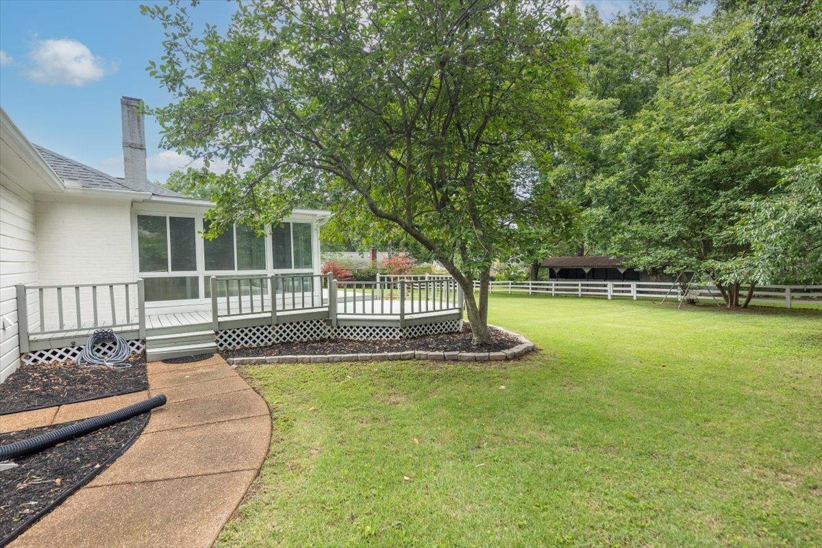 670 Peterson Lake Road Collierville, TN 38017 - Photo 28 of 37 Expansive lawn area featuring a white picket fence, mature trees, and a concrete pathway leading to a screened-in porch with an attached wooden deck