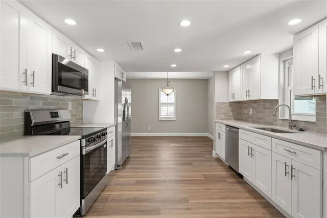 a large kitchen with stainless steel appliances granite countertop a stove top oven a sink dishwasher and a oven with wooden floor