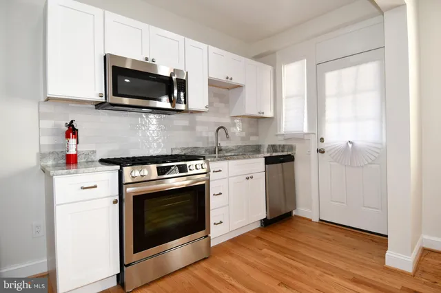 a kitchen with granite countertop a refrigerator stove and white cabinets