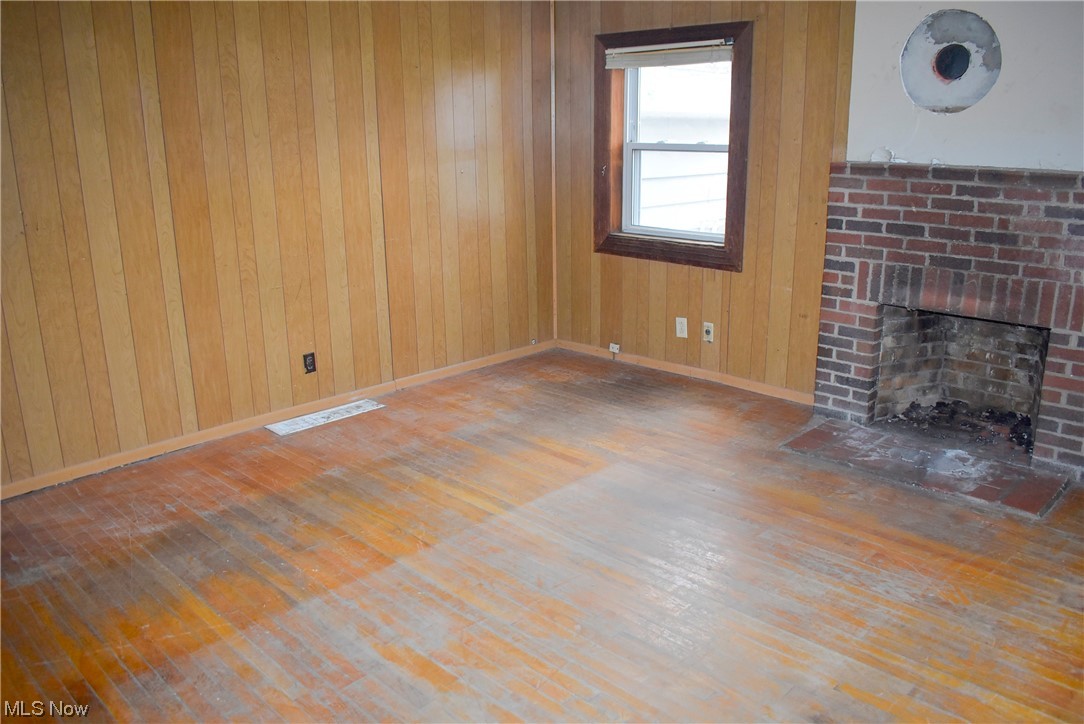 8718 Freedom Road Windham, OH 44288 - Photo 4 of 20 Unfurnished living room featuring dark hardwood / wood-style flooring, a brick fireplace, and wooden walls