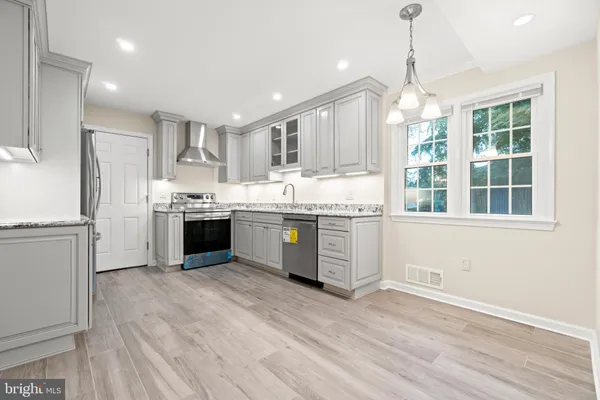 a kitchen with stainless steel appliances granite countertop a stove a sink dishwasher a refrigerator and white cabinets with wooden floor