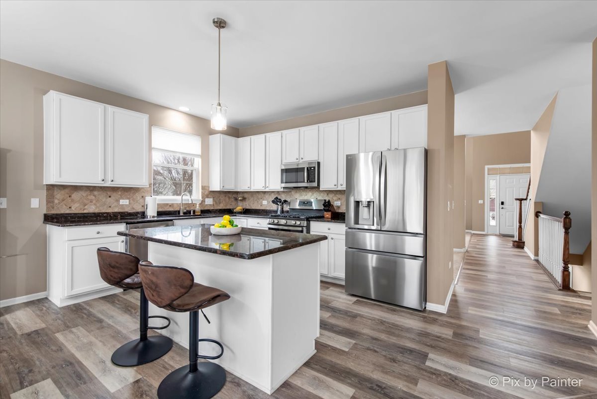 26428 Rustling Birch Way Plainfield, IL 60585 - Photo 3 of 49 a kitchen with kitchen island a refrigerator a stove a dining table and chairs with wooden floors