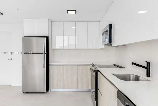 a kitchen with stainless steel appliances a sink a refrigerator a window and cabinets