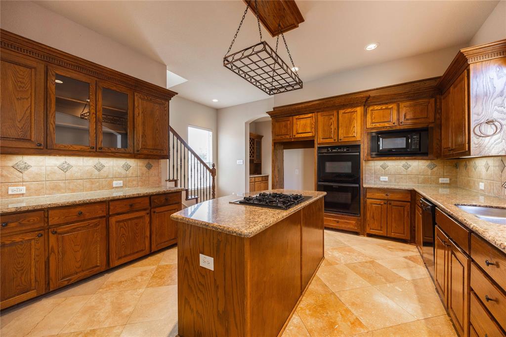 2009 Briarbrook Lane Allen, TX 75002 - Photo 8 of 40 Kitchen featuring backsplash, brown cabinets, arched walkways, a center island, and light stone countertops