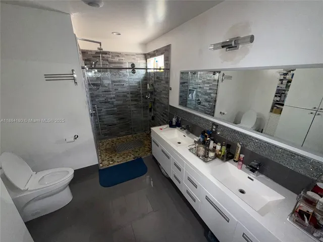 a bathroom with a double vanity sink a toilet and shower