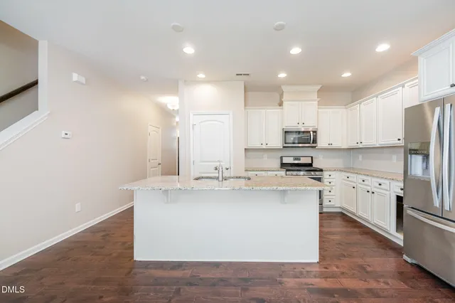 a kitchen with stainless steel appliances granite countertop a sink a stove a refrigerator and white cabinets