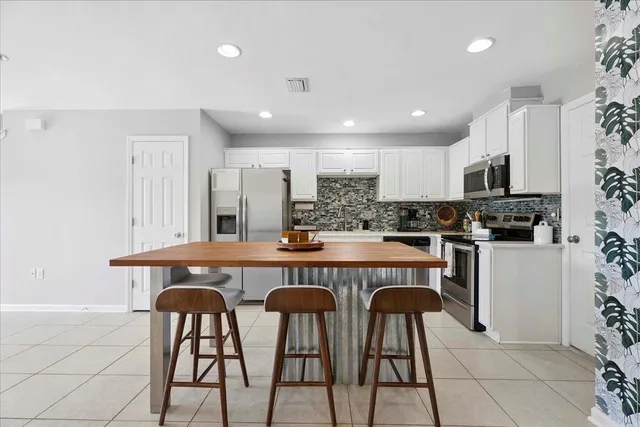 a kitchen with stainless steel appliances a dining table chairs refrigerator and microwave