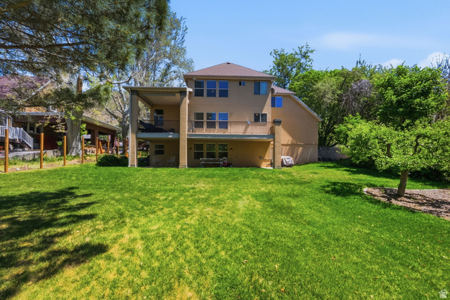 1683 North Main Street Centerville, UT 84014 - Photo 35 of 37 Expansive grassy yard featuring a multi-story residence with a covered patio, upper-level balcony, multiple large windows, and mature perimeter trees