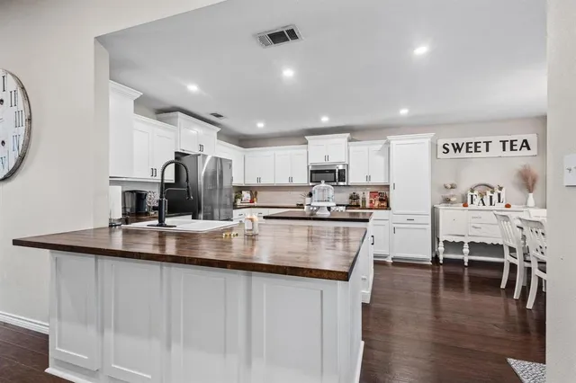 a kitchen with stainless steel appliances granite countertop a refrigerator a sink a stove and white cabinets with wooden floor