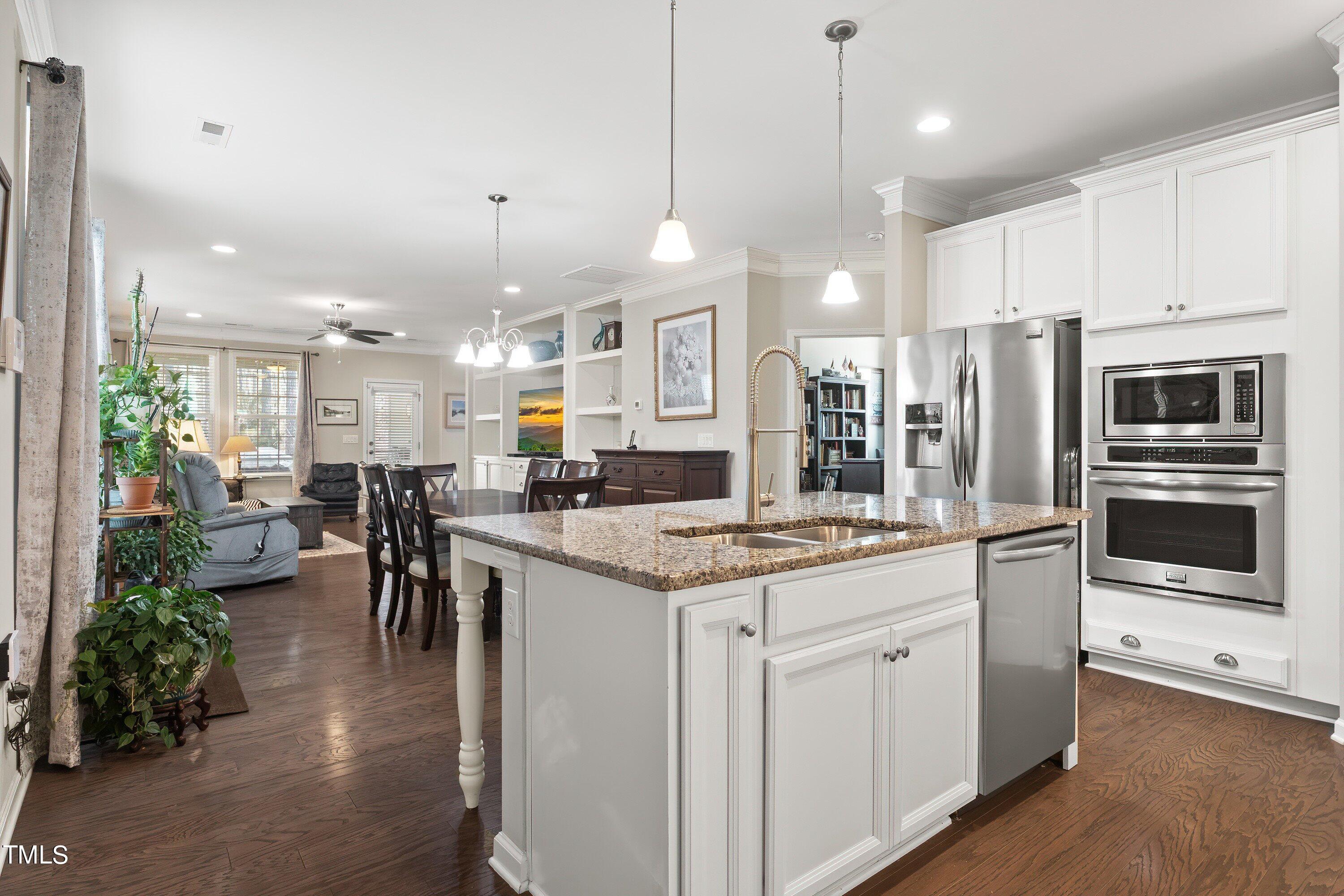 a kitchen with stainless steel appliances kitchen island granite countertop a large island a stove a refrigerator a sink a dining table and chairs with wooden floor