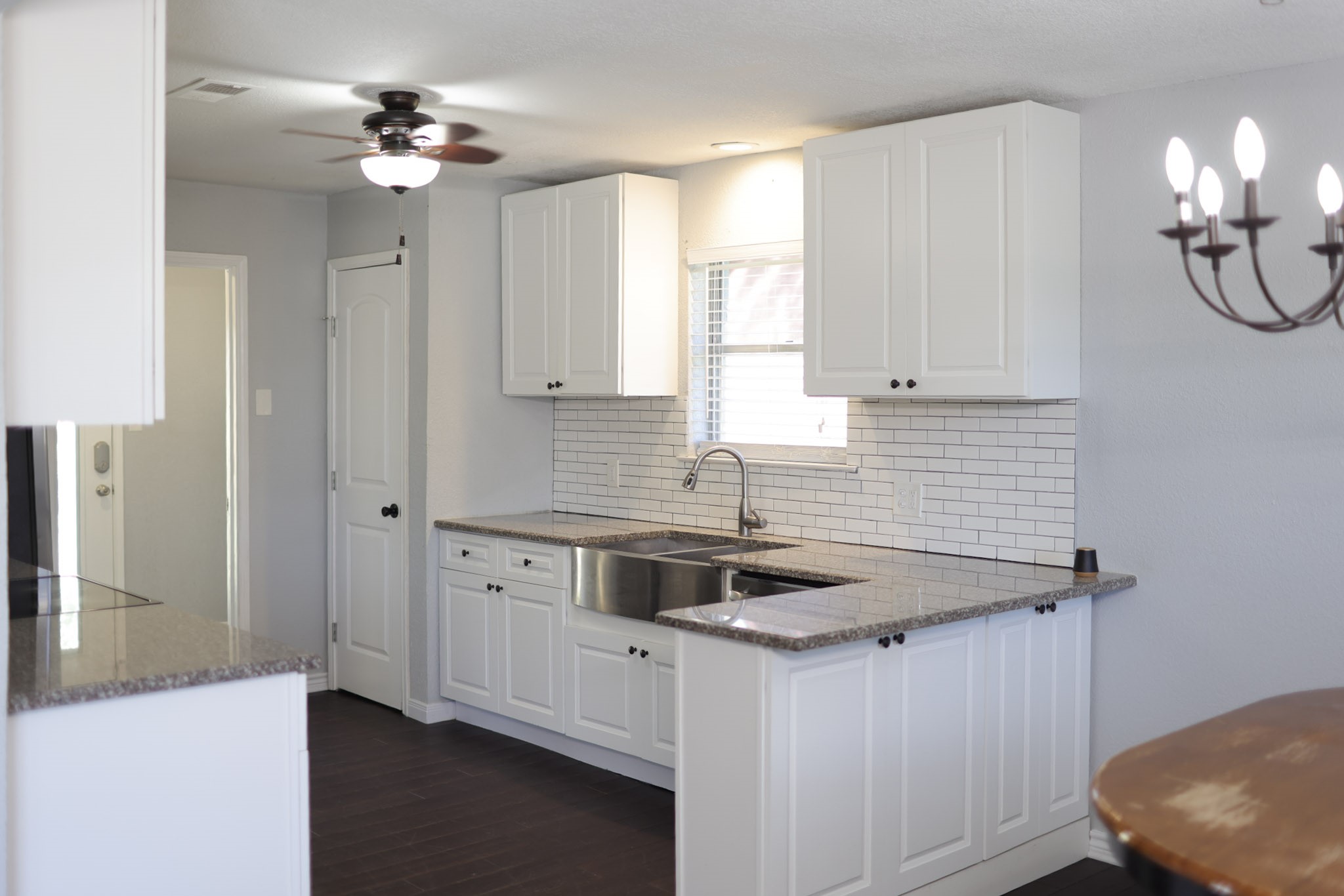 407 Tamarind Street Lake Jackson, TX 77566 - Photo 20 of 36 Bright and modern kitchen featuring white cabinetry, granite countertops, and a subway tile backsplash. Includes a stainless steel sink, ceiling fan, and adjacent dining area with a stylish chandelier.
