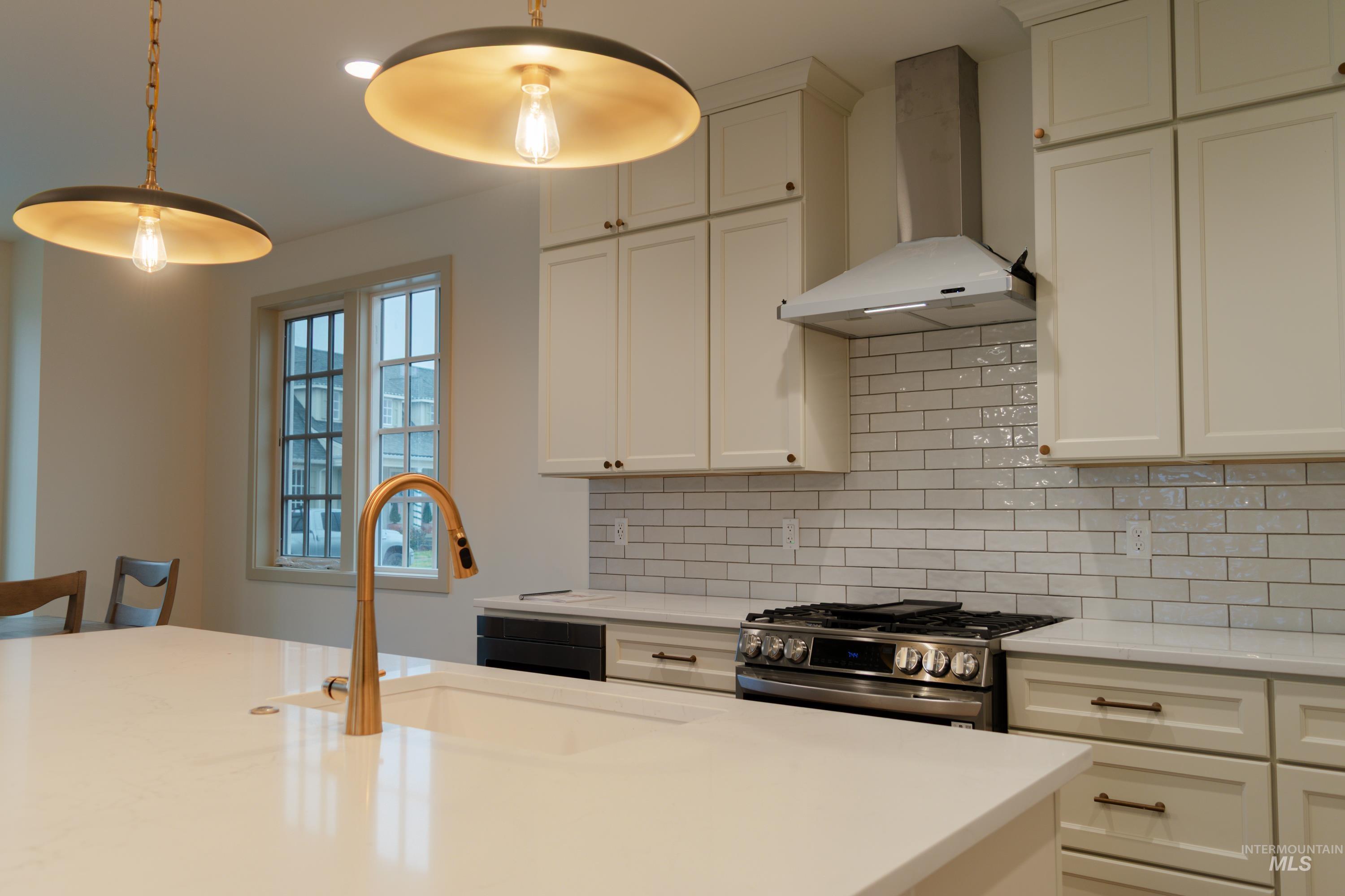 1560 Slonaker, Unit ONYX Moscow, ID 83843 - Photo 11 of 49 Kitchen featuring wall chimney range hood, stainless steel gas stove, tasteful backsplash, light stone counters, and decorative light fixtures