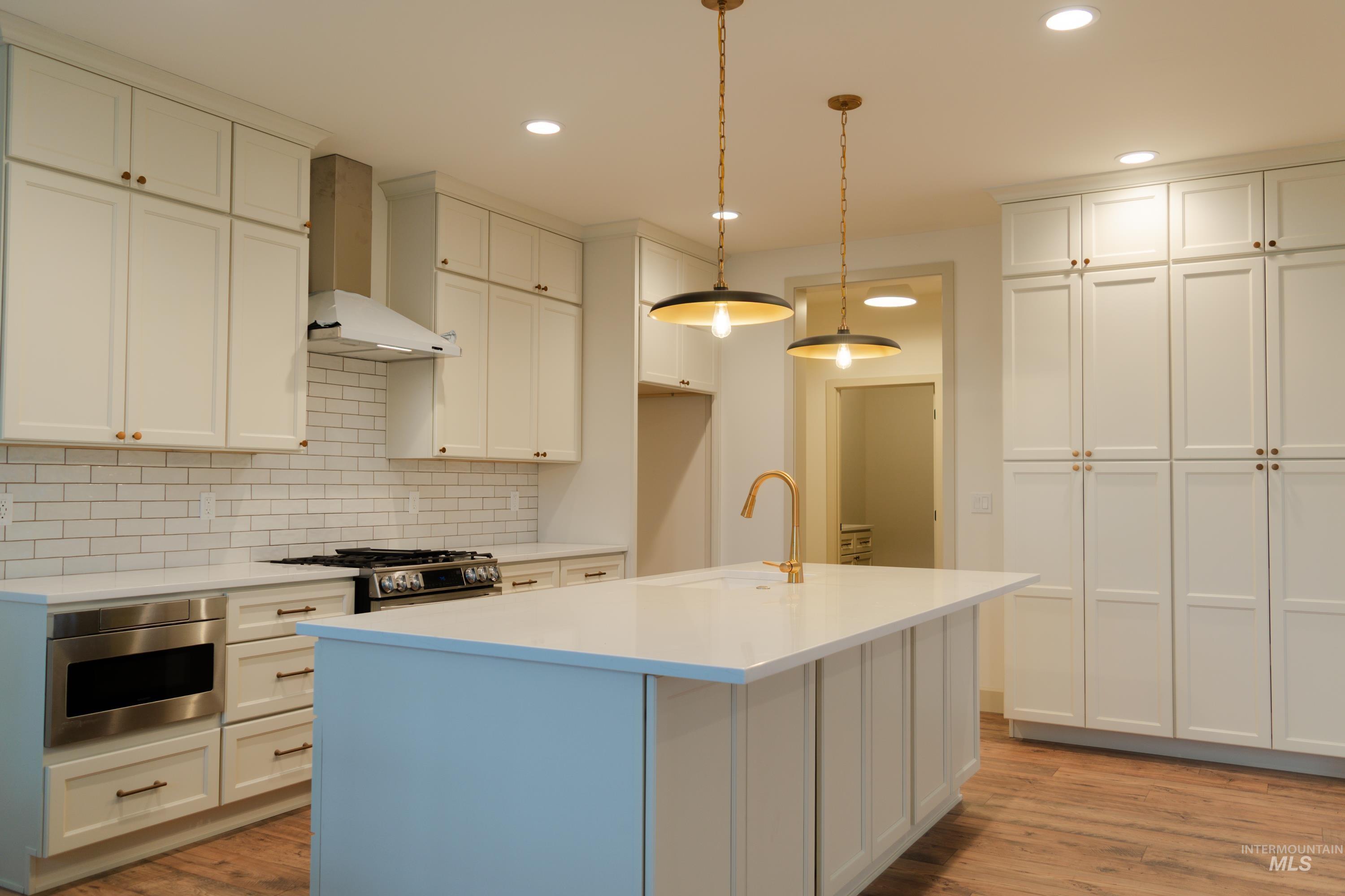 1560 Slonaker, Unit ONYX Moscow, ID 83843 - Photo 12 of 49 Kitchen with wall chimney range hood, hanging light fixtures, light wood-type flooring, appliances with stainless steel finishes, and tasteful backsplash