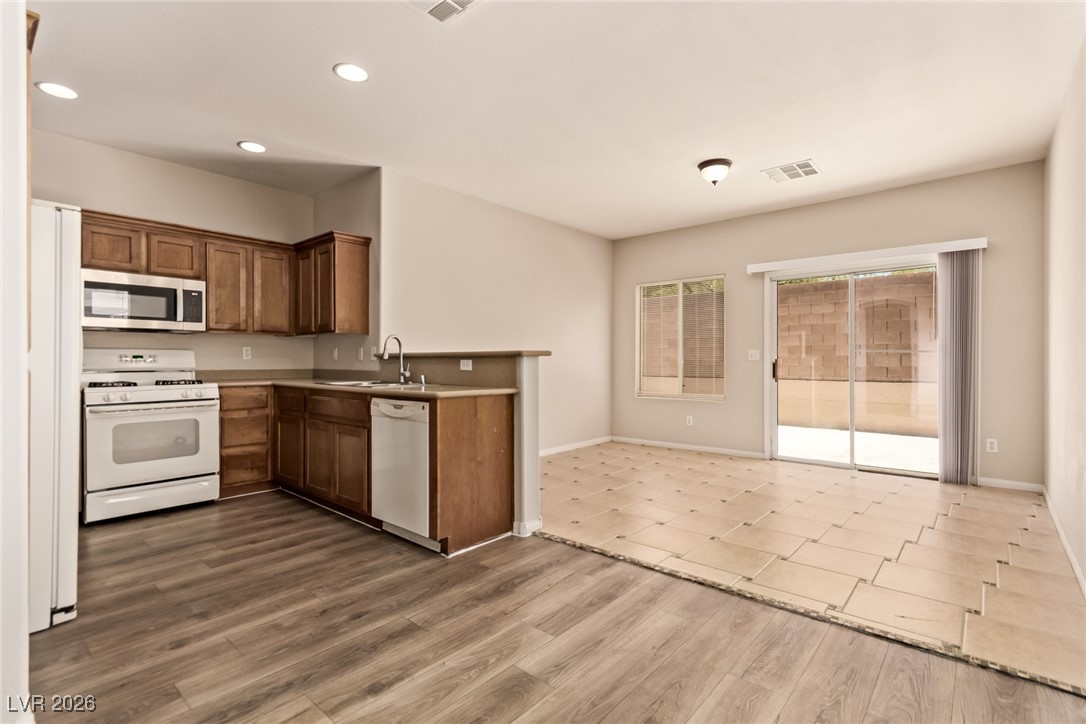 6224 Boulder Rise Street North Las Vegas, NV 89115 - Photo 10 of 27 Kitchen with white appliances, brown cabinets, a peninsula, dark wood-style flooring, and light countertops