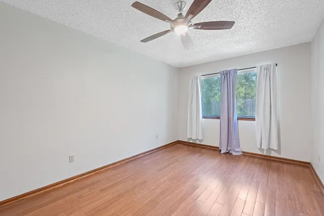 an empty room with wooden floor fan and windows