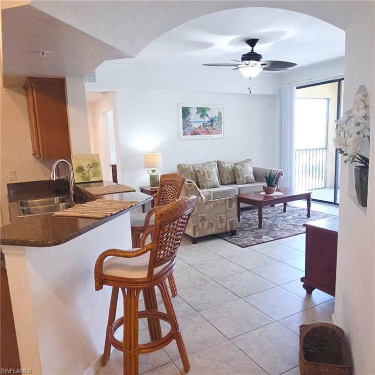 12975 Positano Circle, Unit 207 Naples, FL 34105 - Photo 4 of 24 Living area featuring arched walkways, light tile patterned flooring, and a ceiling fan