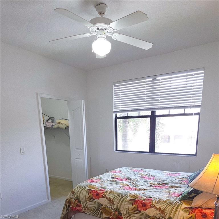 12975 Positano Circle, Unit 207 Naples, FL 34105 - Photo 9 of 24 Bedroom featuring a spacious closet, ceiling fan, and light colored carpet
