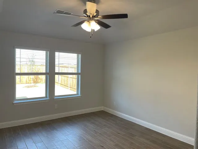 an empty room with wooden floor fan and windows