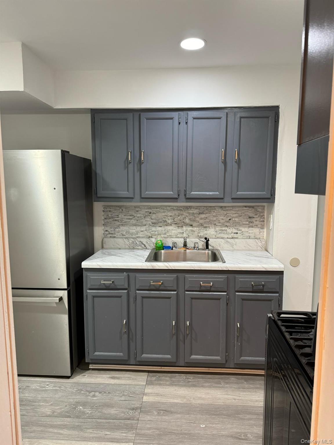 114-25 201st Street Queens, NY 11412 - Photo 2 of 18 Kitchen with gray cabinets, freestanding refrigerator, light countertops, backsplash, and black gas range oven