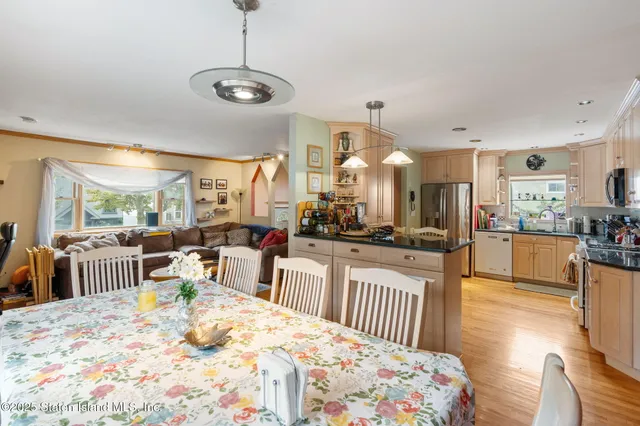a kitchen with stainless steel appliances kitchen island granite countertop a refrigerator a sink dishwasher a dining table and chairs with wooden floor