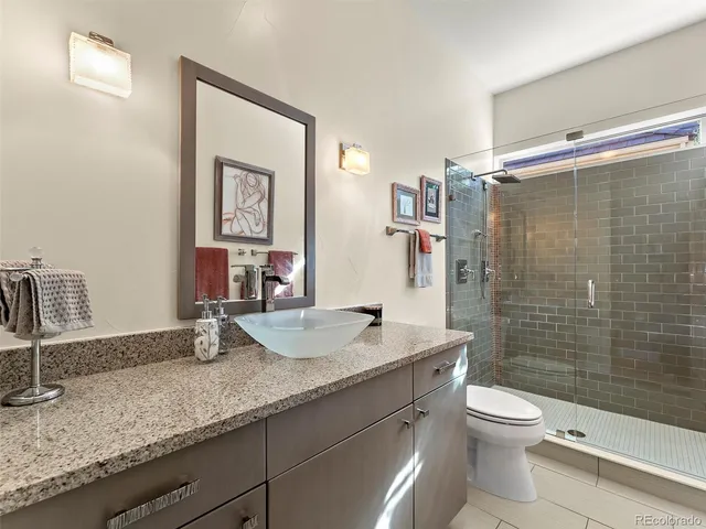 a bathroom with a granite countertop sink a toilet a mirror and shower