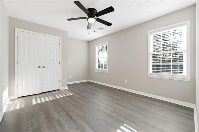 an empty room with wooden floor ceiling fan and windows