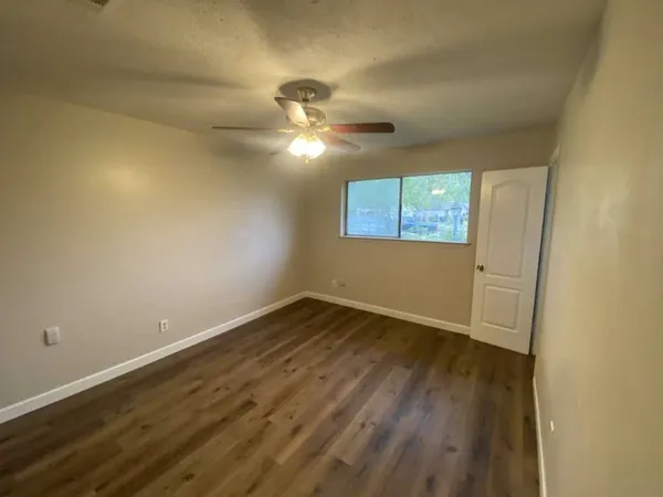 an empty room with wooden floor fan and windows