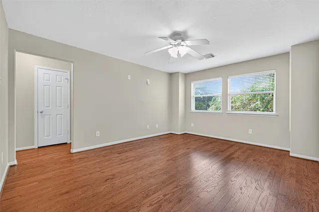 an empty room with wooden floor chandelier fan and windows