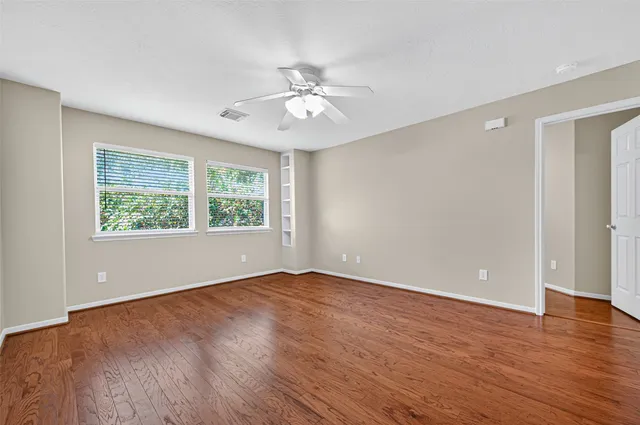 a view of an empty room with wooden floor and a ceiling fan
