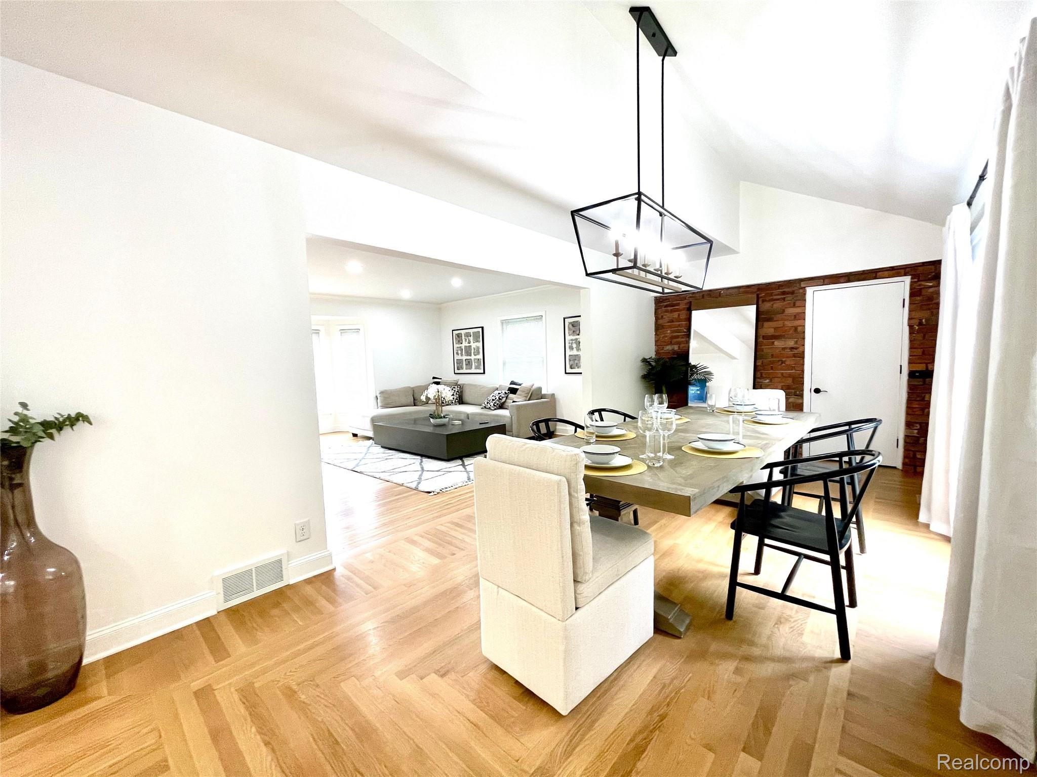 60 Devon Road Bloomfield Hills, MI 48302 - Photo 20 of 50 Dining area featuring herringbone wood-finish flooring, a vaulted ceiling, exposed brick accent wall, and a contemporary linear chandelier
