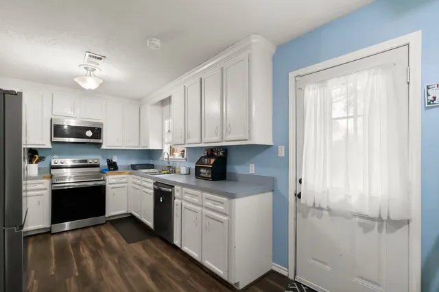 a kitchen with granite countertop a refrigerator a sink dishwasher a stove and white cabinets with wooden floor