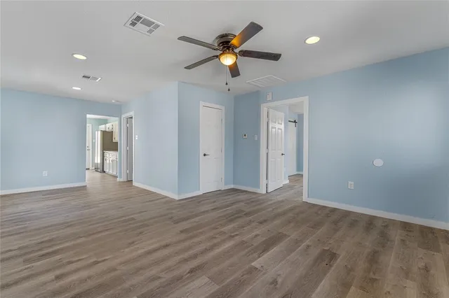 a view of an empty room with wooden floor and a ceiling fan